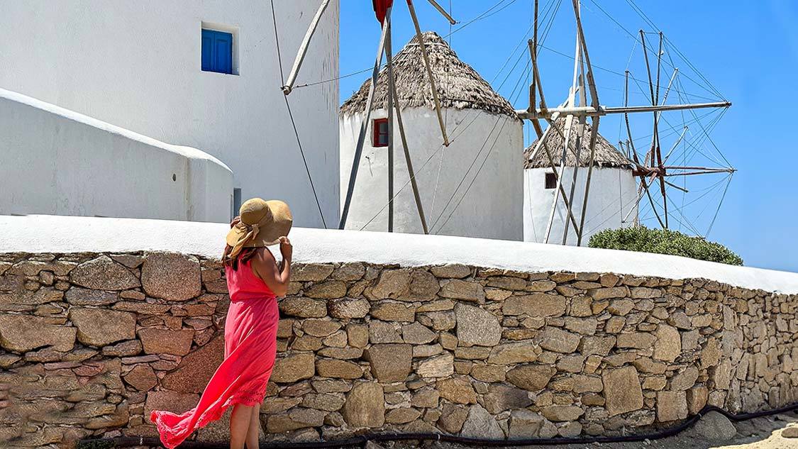 A woman in a pink dress looks at windmills during one day on Mykonos