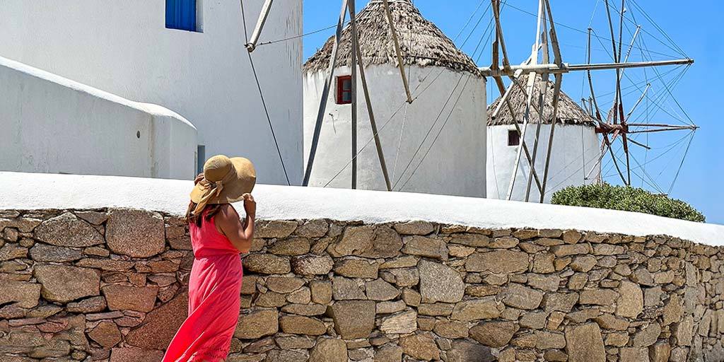 A woman in a pink dress looks at windmills during one day on Mykonos