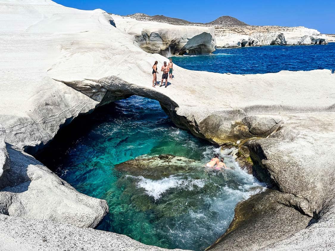 visitors swim under the rock arches of Sarakiniko Beach