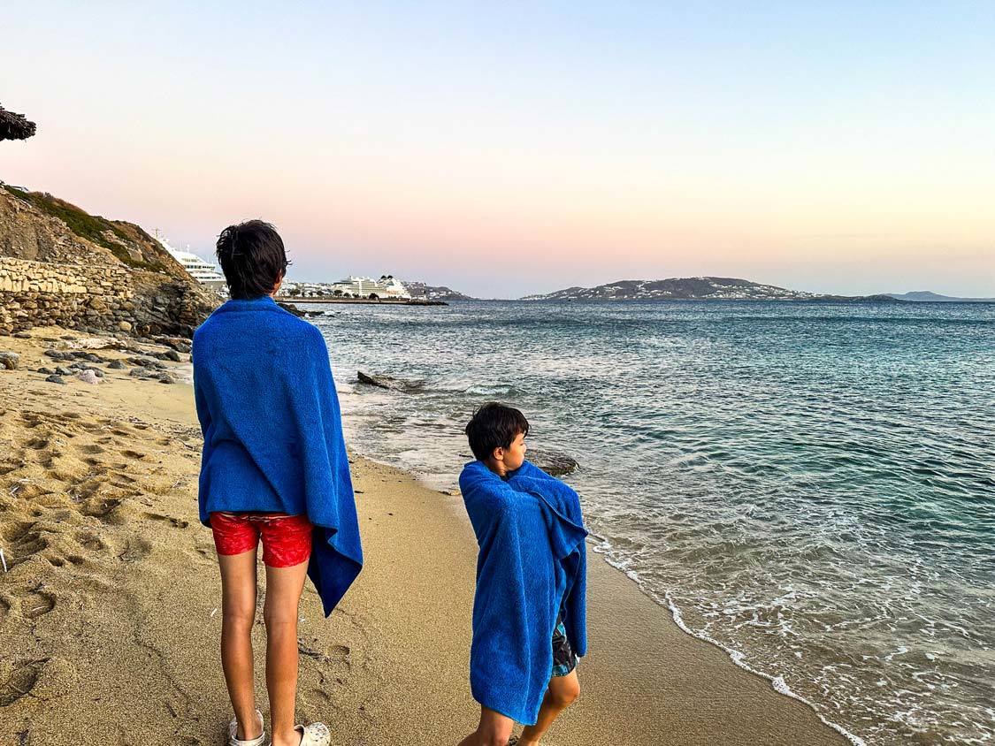 Two boys look out over the water at a cruise ship port from Agio Stephano Beach