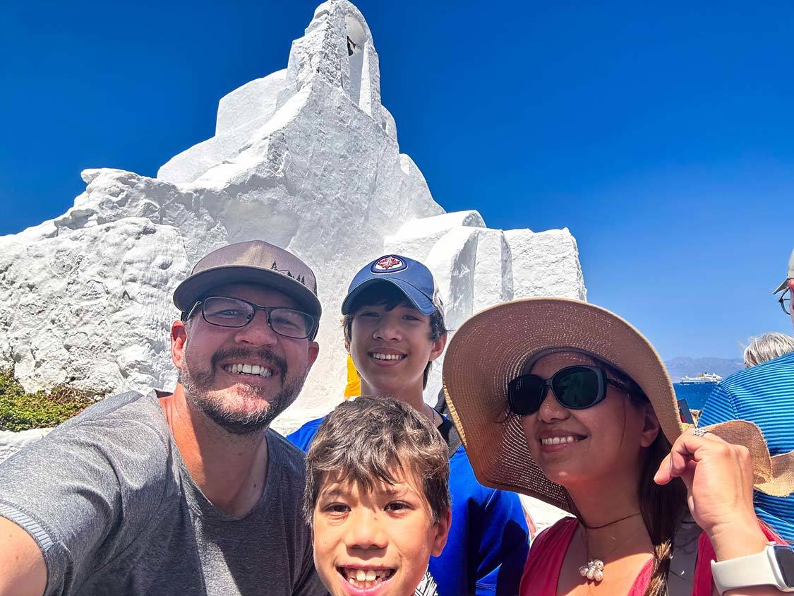 A mixed race travel family smiles in front of a church in Chora, Mykonos