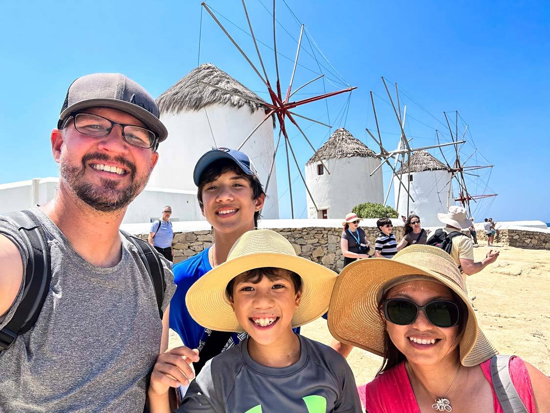 A family smiles for a selfie in front of the Mykonos windmills