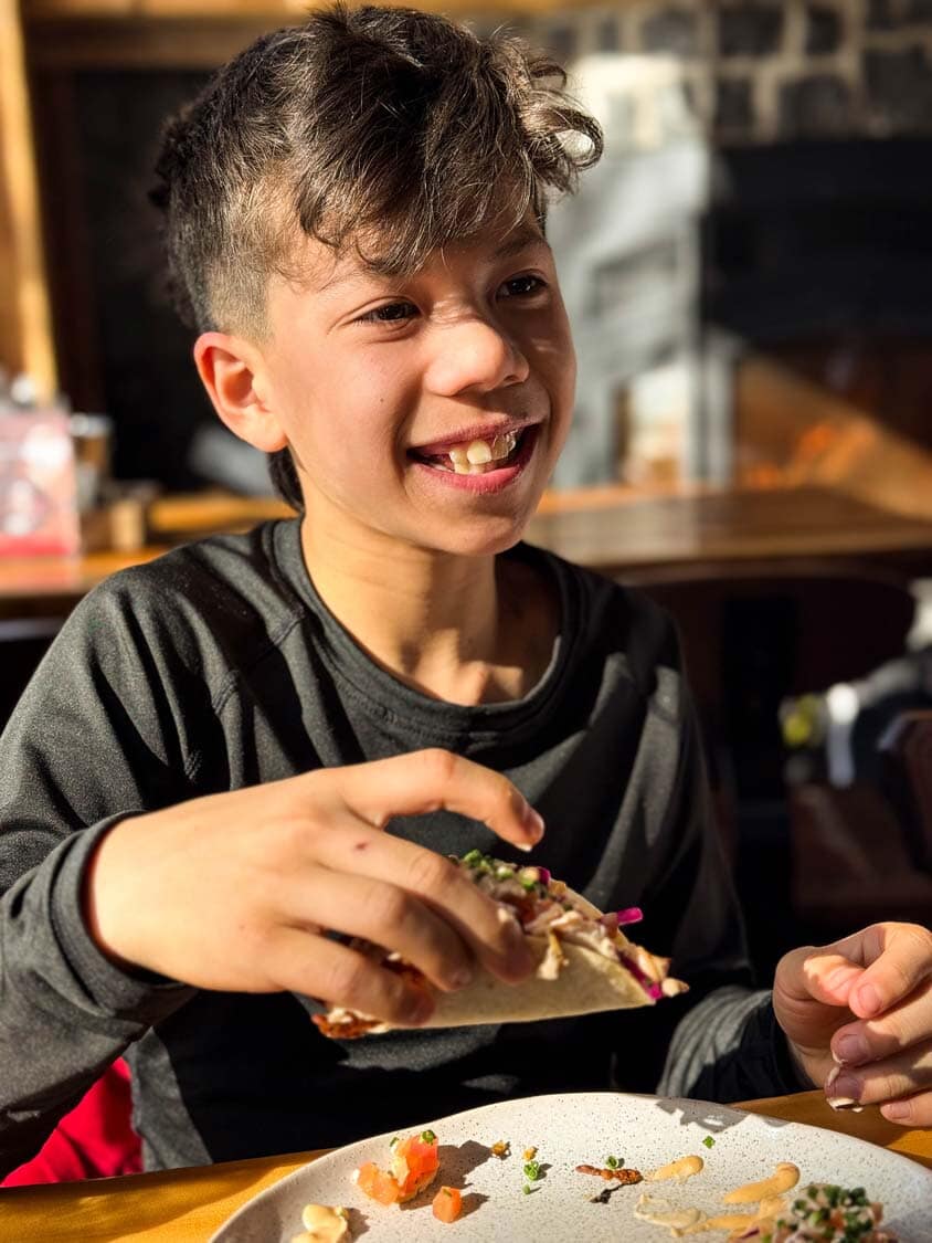 A smiling boy eats nachos in a cabin at 2800 du Parc, Shawinigan