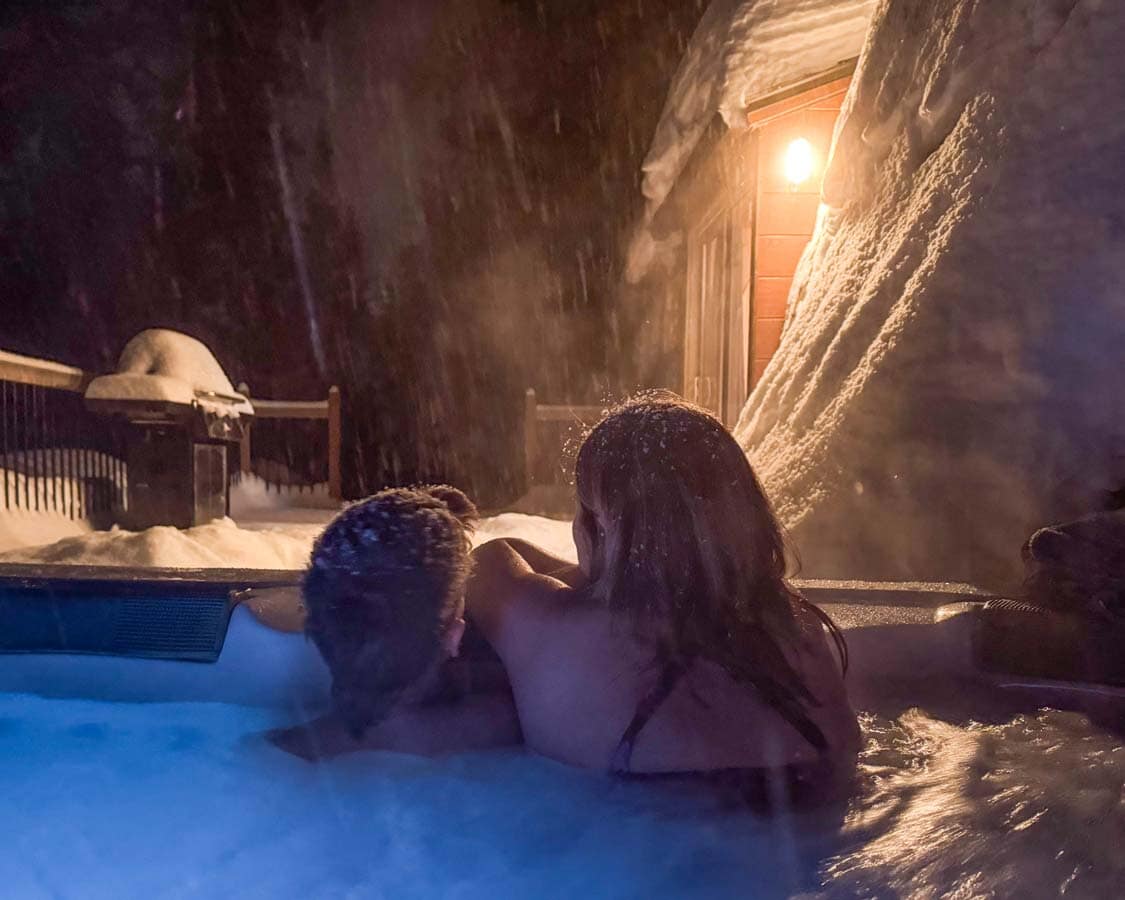 A mother and sun enjoy an outdoor hot tub in the snow