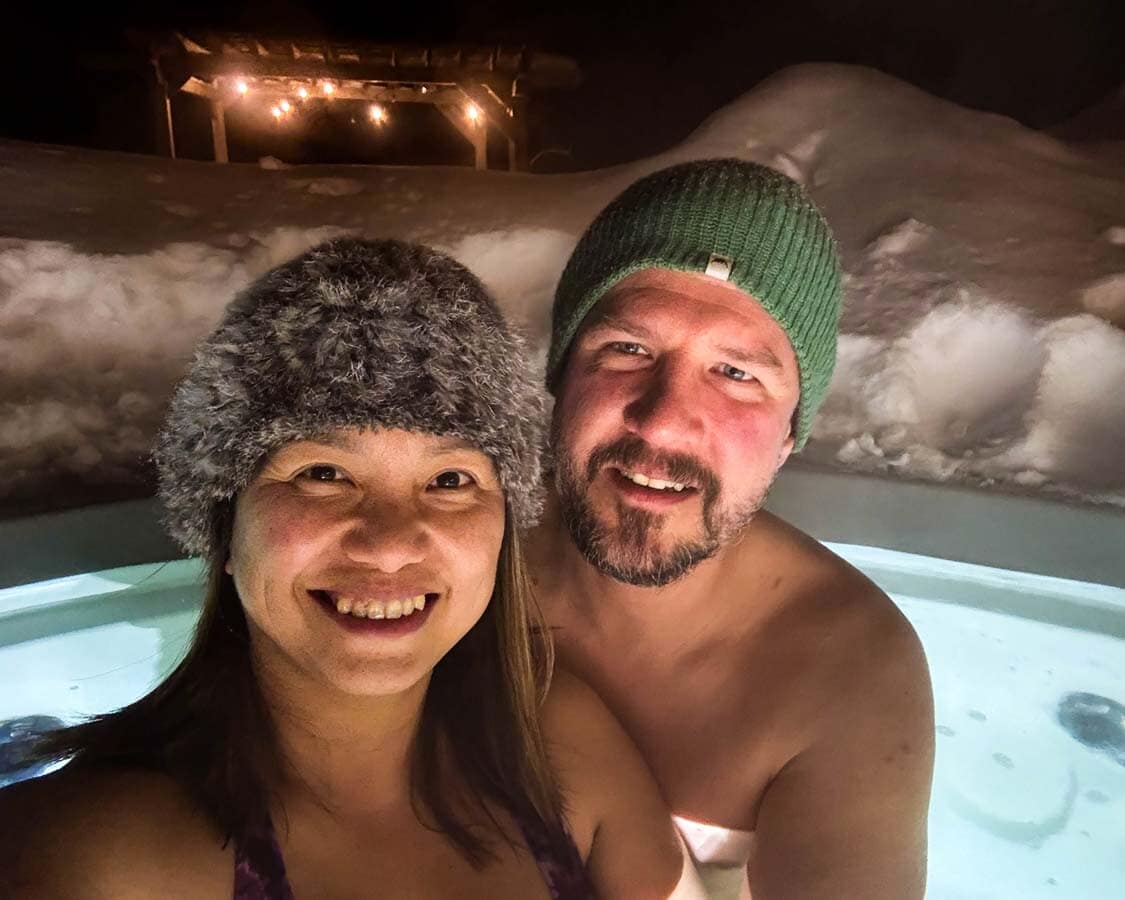 A couple wearing toques relax in a an outdoor hot tub at Auberge du Vieux Moulin in the winter