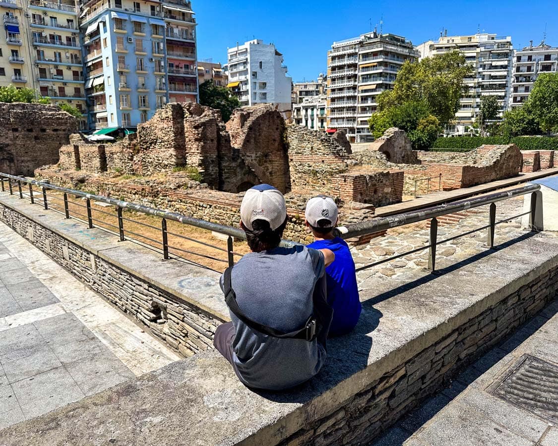 Two boys sit on a bench overlooking the Palace of Galerius in Thessaloniki, Greece