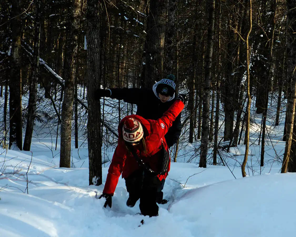 Two people struggling up a slippery slope while winter hiking in La Mauricie National Park