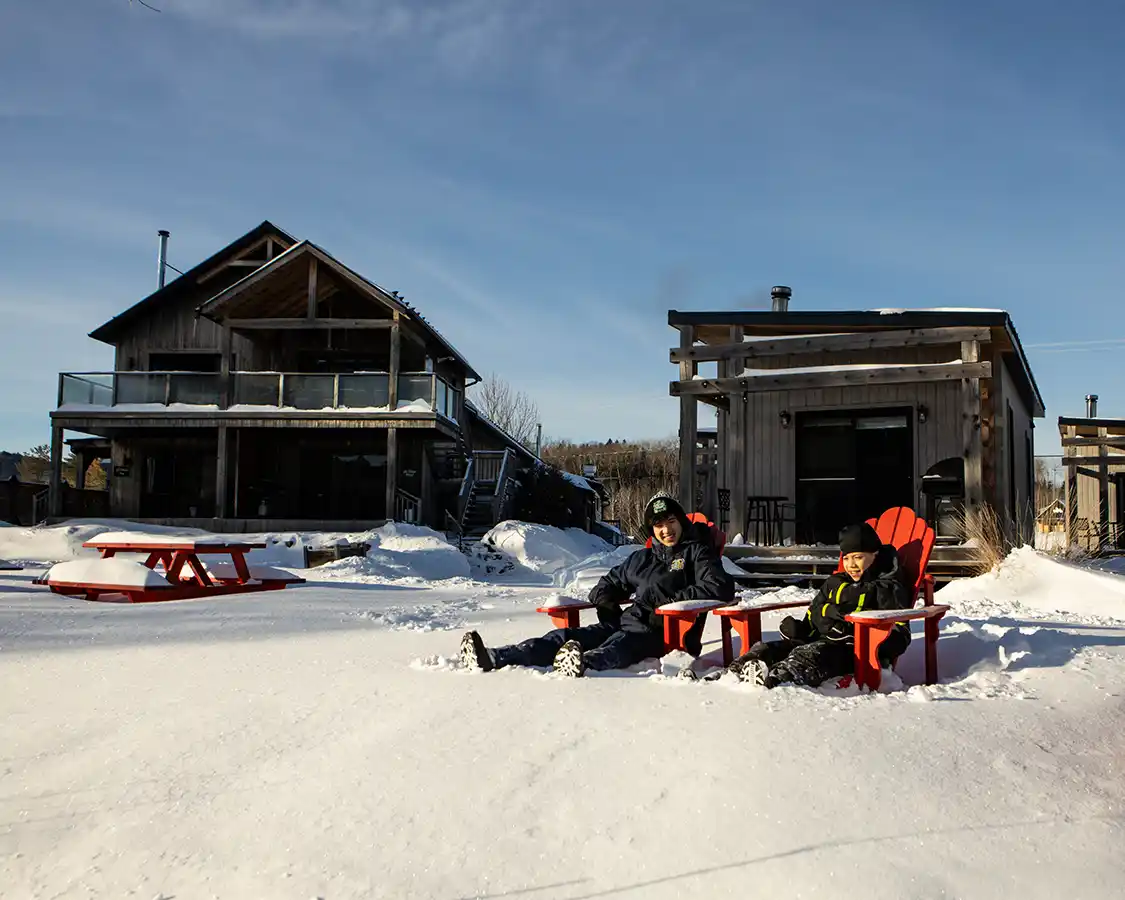 Two boys sit in chairs in the deep snow at 2800 du Parc cabin