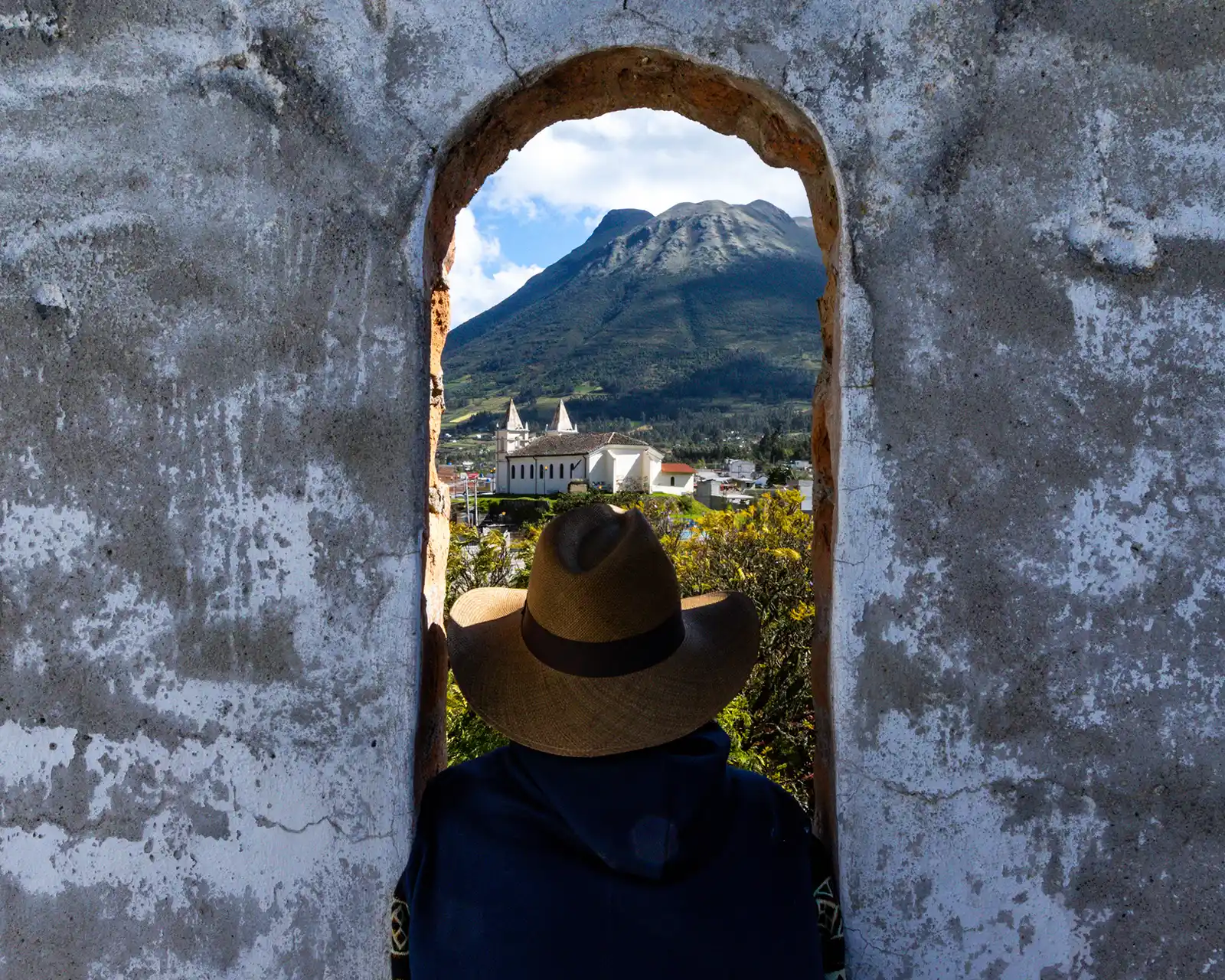 A boy wearing a Panama hat gazes out from the bell tower at Hacienda Cusin