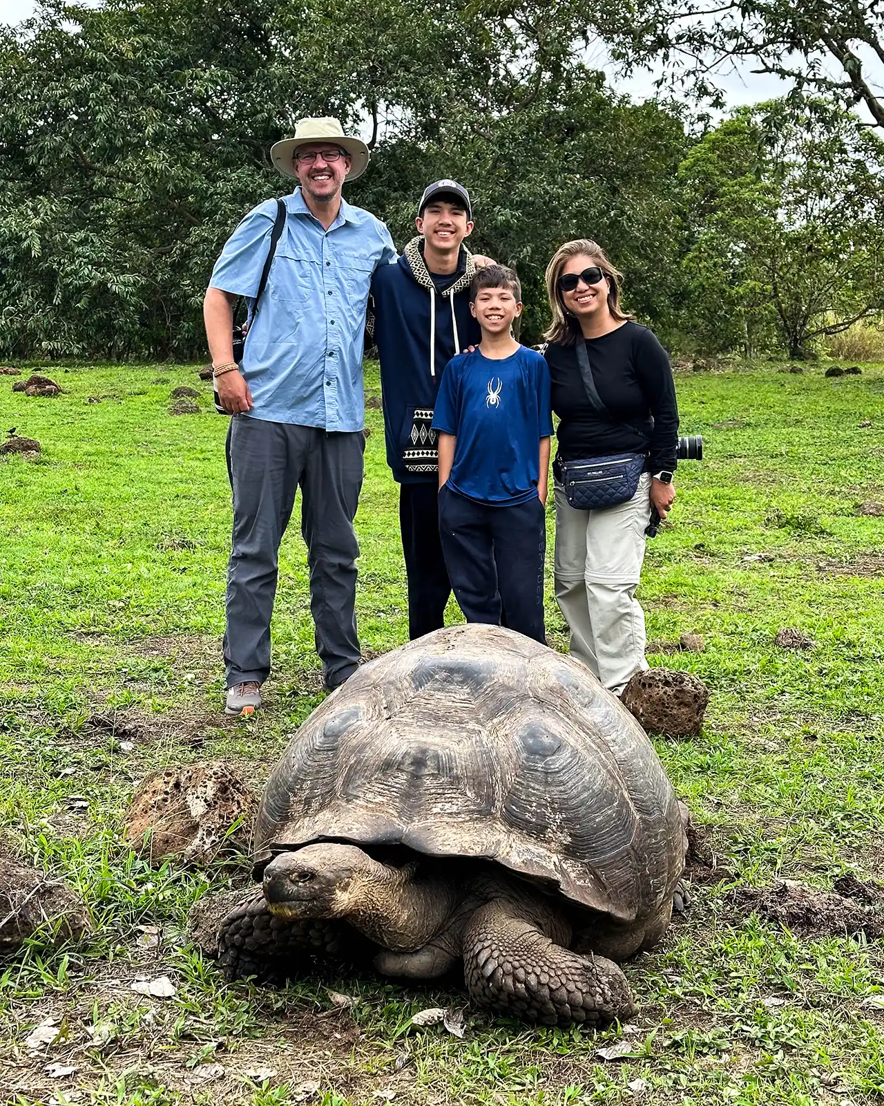 A family poses with a wild giant tortoise at El Chat Reserve on Santa Cruz Island Galapagos