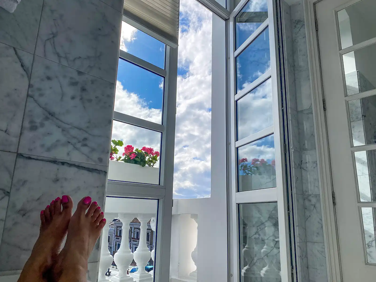 Woman's feet resting on the edge of a bathtub next to a tall window with flowers at Casa Gagontea,, Quito