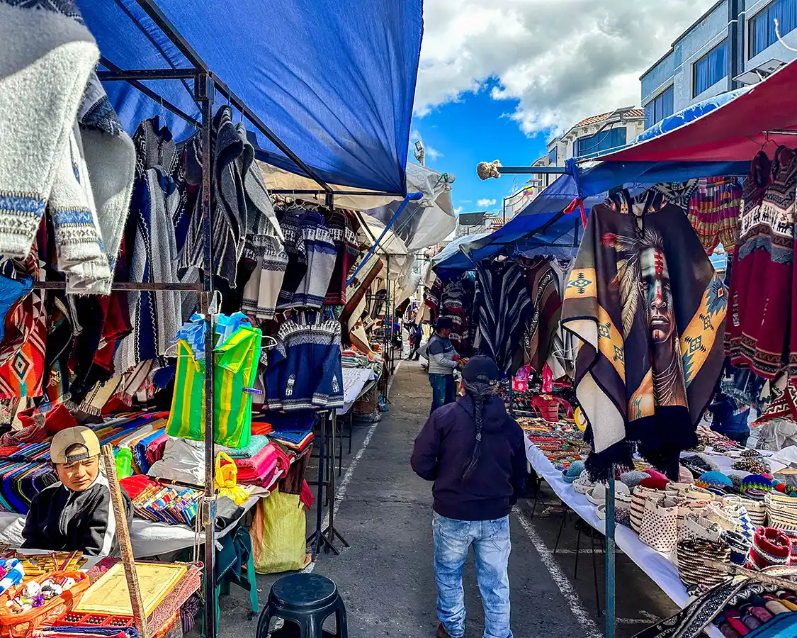 A Kichwa man walks through colorful displays at the Otavalo market