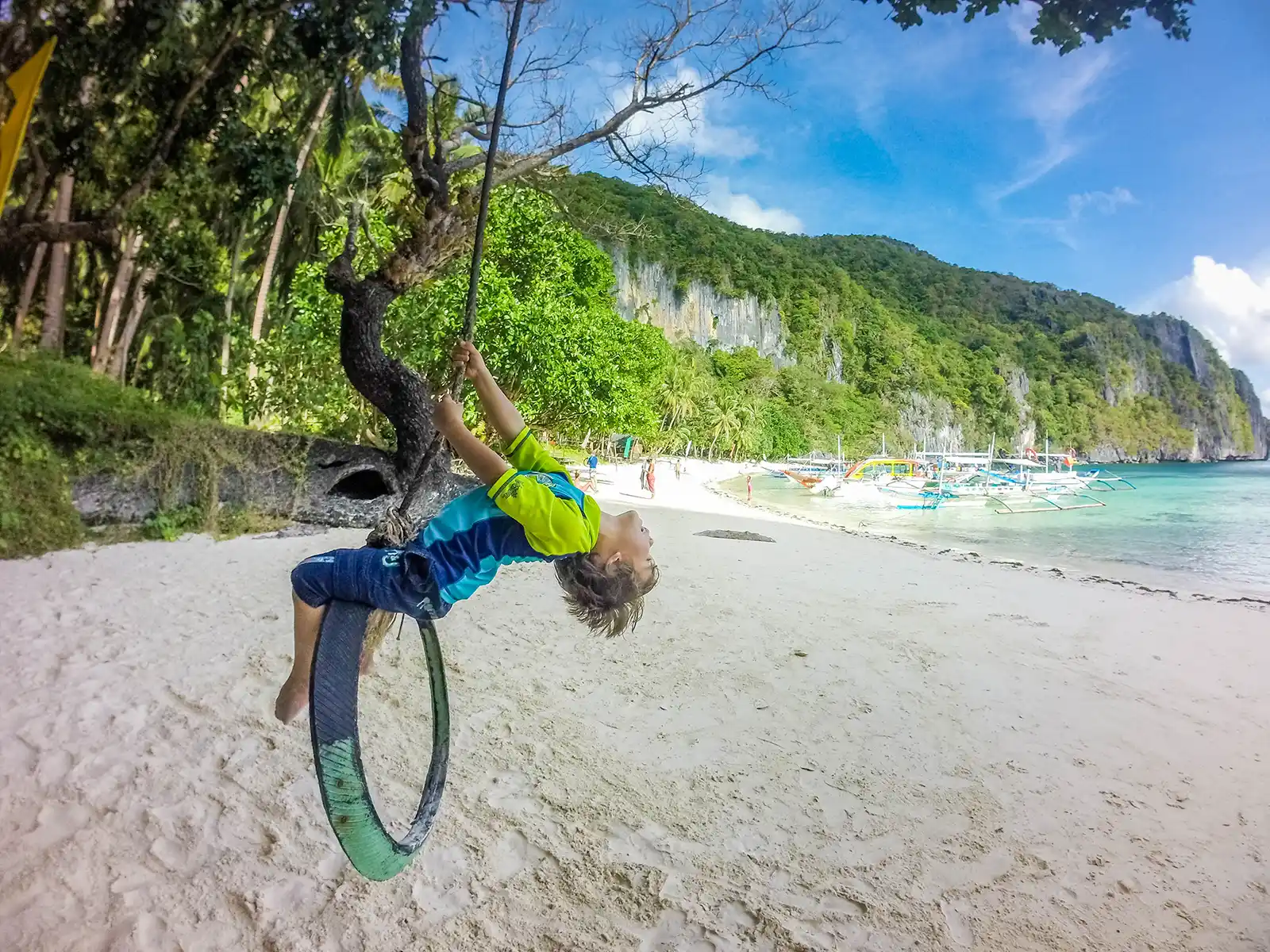 A young boy plays on a rope swing on a beach in the Philippines