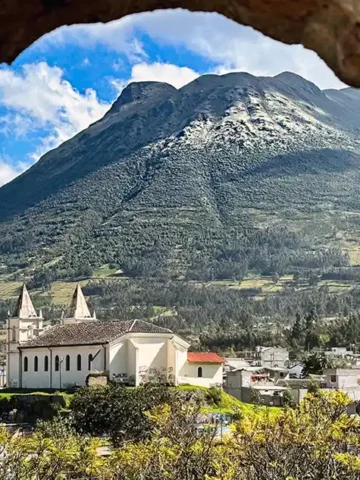 A small town and church lie next to a lush mountain as seen through a stone window frame in Otavalo, Ecuador.