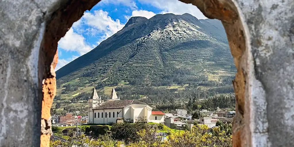 A small town and church lie next to a lush mountain as seen through a stone window frame in Otavalo, Ecuador.