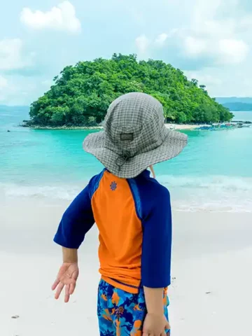 A young boy in swimwear looks out at an island in the ocean