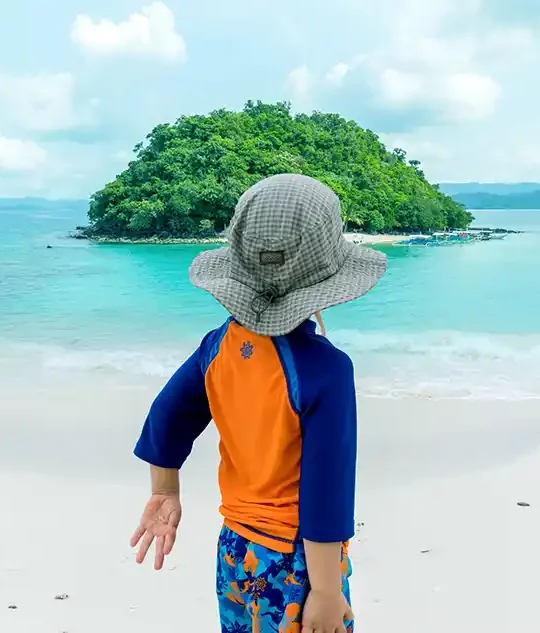 A young boy in swimwear looks out at an island in the ocean
