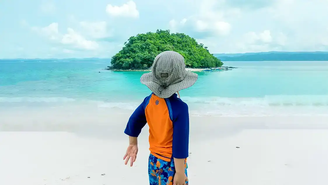 A young boy in swimwear looks out at an island in the ocean
