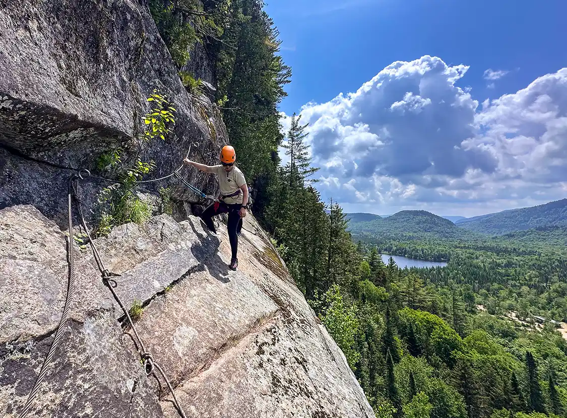 A woman hangs off the side of a cliff on a via ferrata near Quebec City