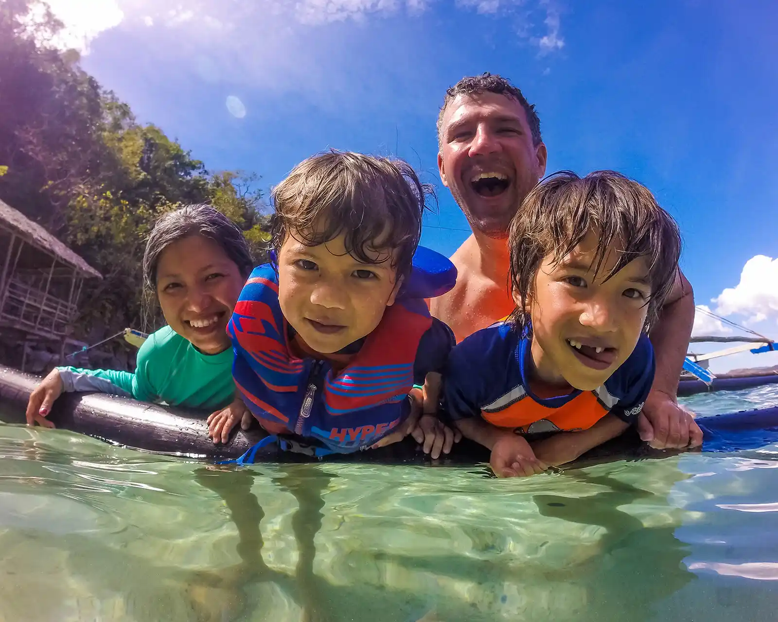 A smiling family hangs off the outrigger of a bangka in the Philippines