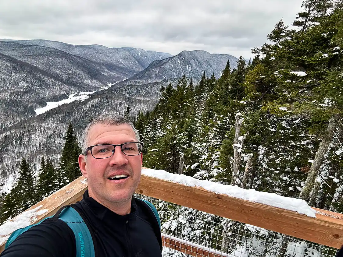A man poses for a selfie overlooking a valley while winter hiking in Jacques Cartier National Park