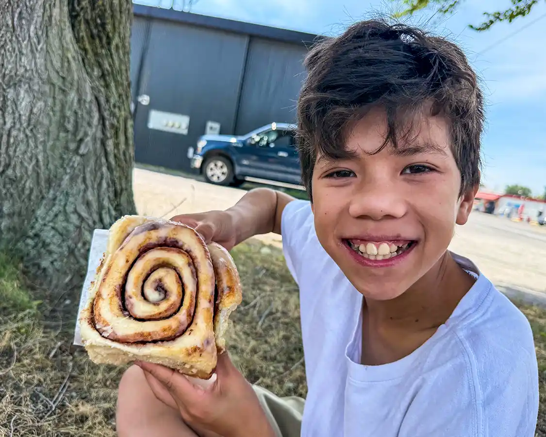 A boy holds up a cinnamon bun the size of his head from Wannamaker's Bakeshop