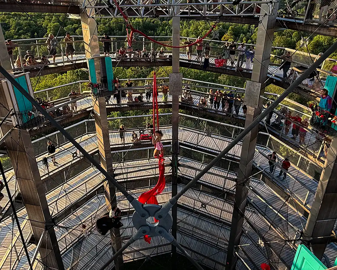 An aerial acrobat hangs from a silk cloth in the middle of a tall observation tower in Sentiers des cimes