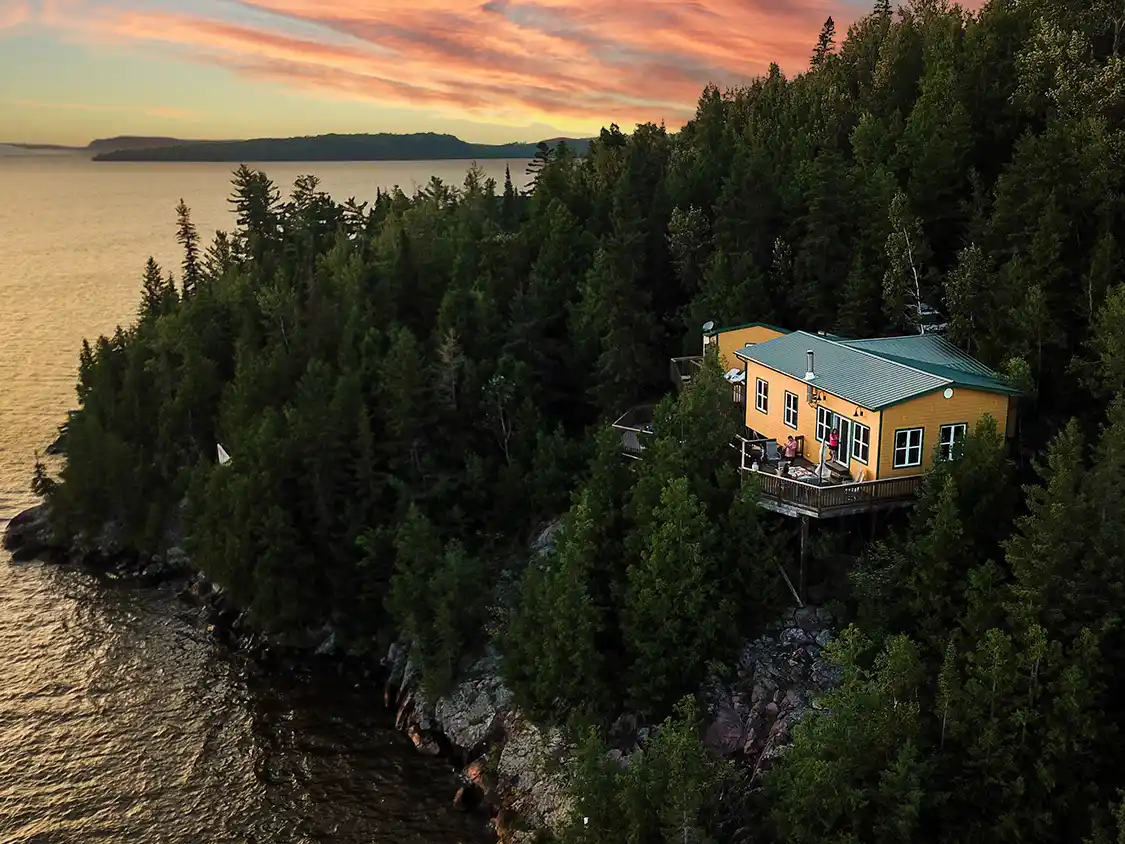 A scenic yellow cottage sits on a hilltop overlooking Lake Temiscamingue at sunset