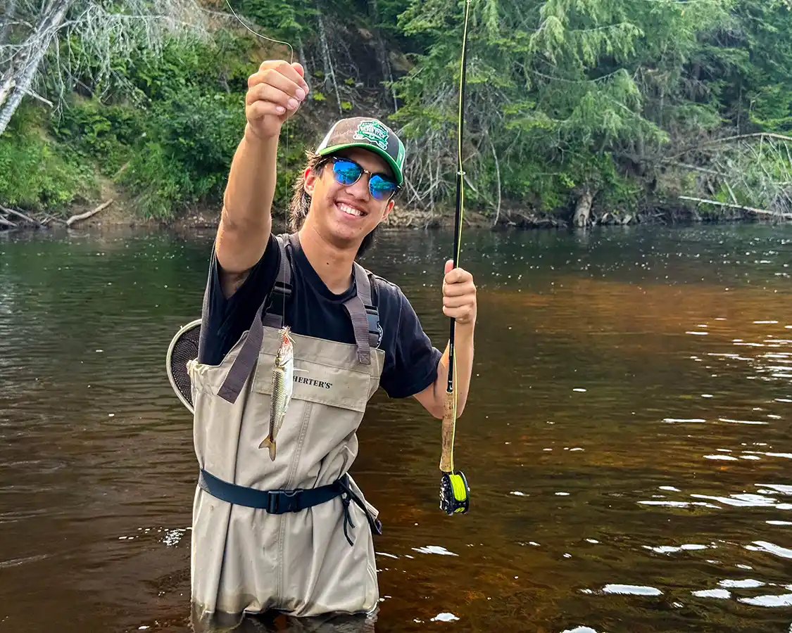 A teenager holds up a fish he caught while fly-fishing in Mont Tremblant in summer