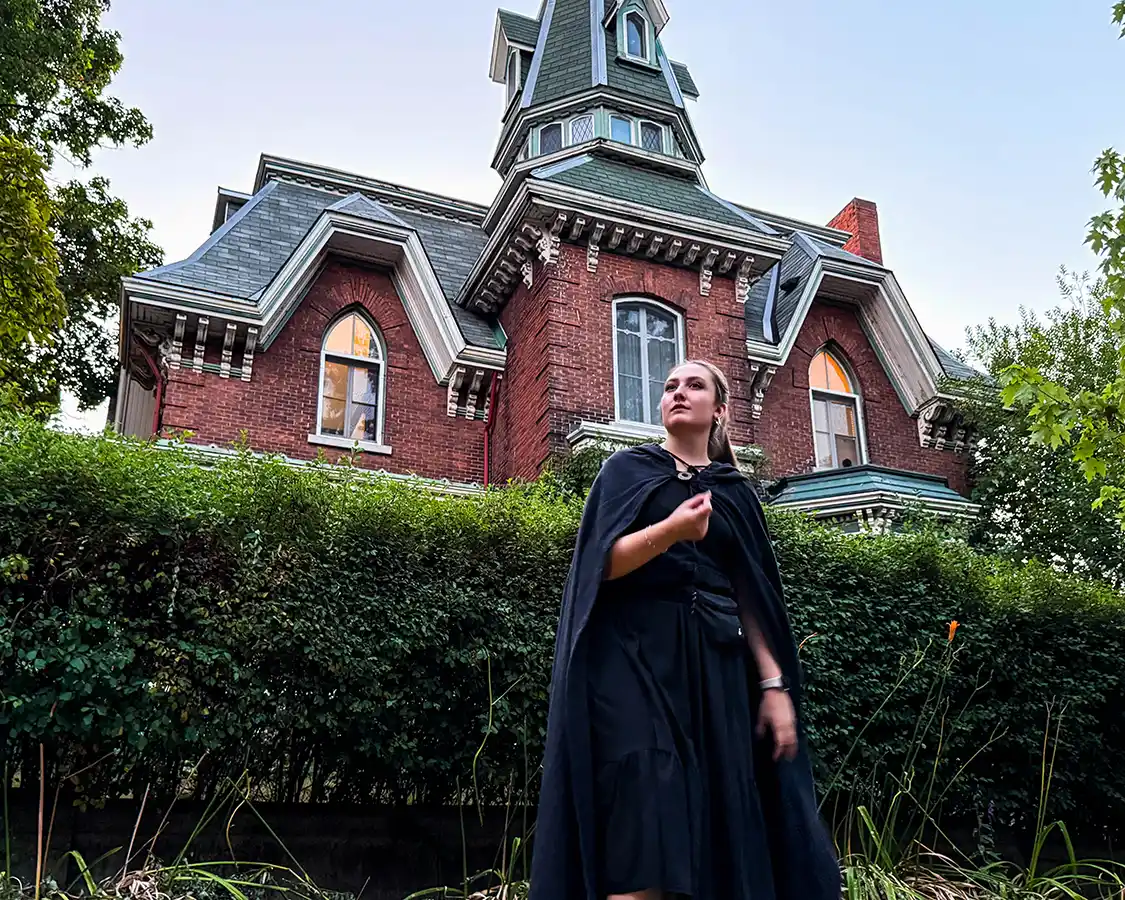 A guide for the Kingston Haunted Walk dressed in black robes stands in front of a spooky-looking inn.
