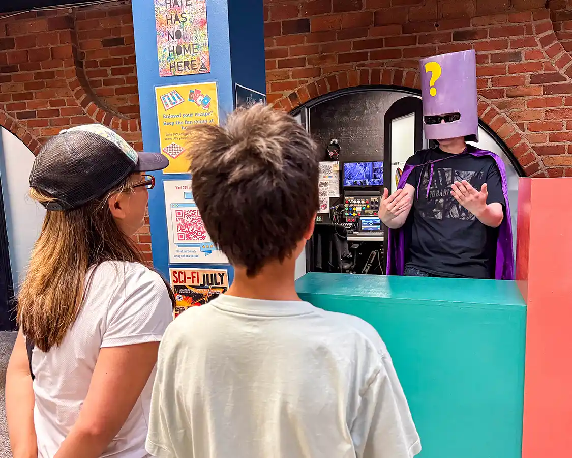 A mother and son laugh while talking to a man dressed as a super villain at Improbable Escapes in Kingston, Ontario.