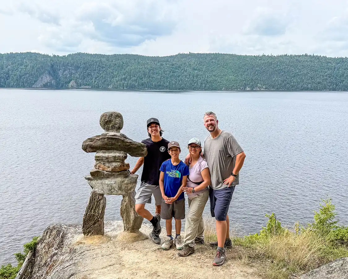 A family poses with an inulshuk on a hiking trail in Parc National d'Opemican