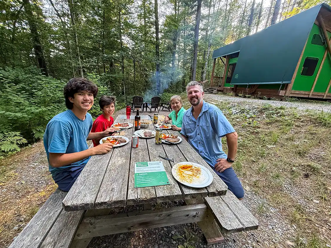 A family eats a meal at a picnic bench in a ready-to-camp site in Parc National d'Opemican