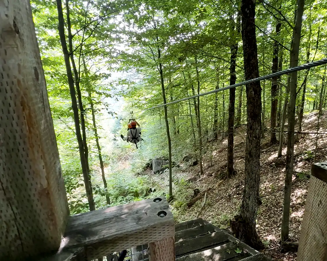 Two boys take a zipline through the trees on a Via Ferrata at TyroParc in Quebec