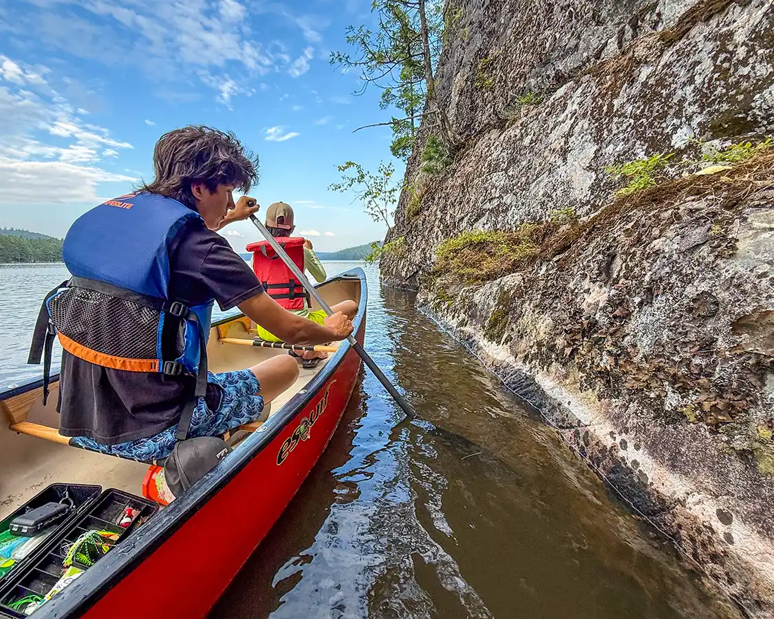Two boys paddle a canoe next to a cliff face on Lake Temiscamingue