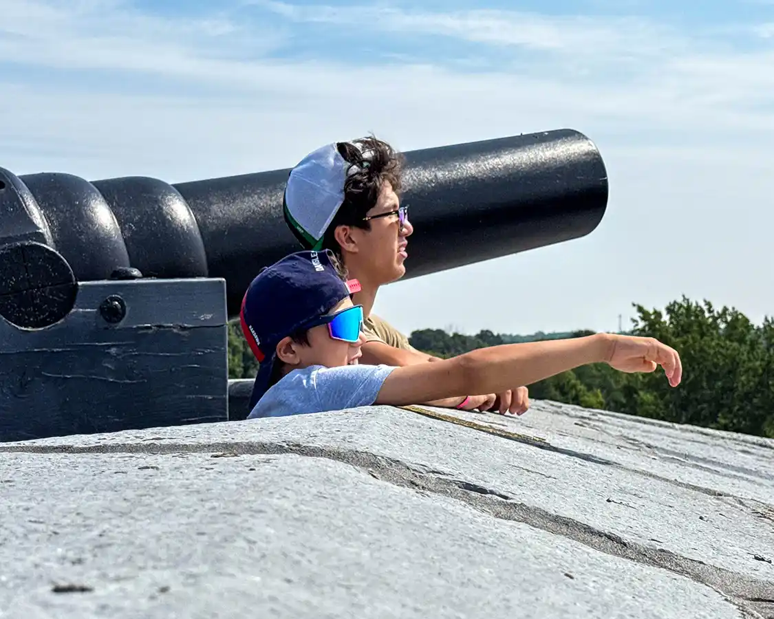 Two boys look out from a battlement at Fort Henry, the younger one points out at the waters of Lake Ontario