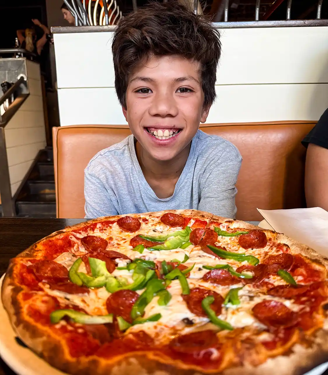 A young boy smiles over a large pizza at Wooden Heads restaurant in Kingston.