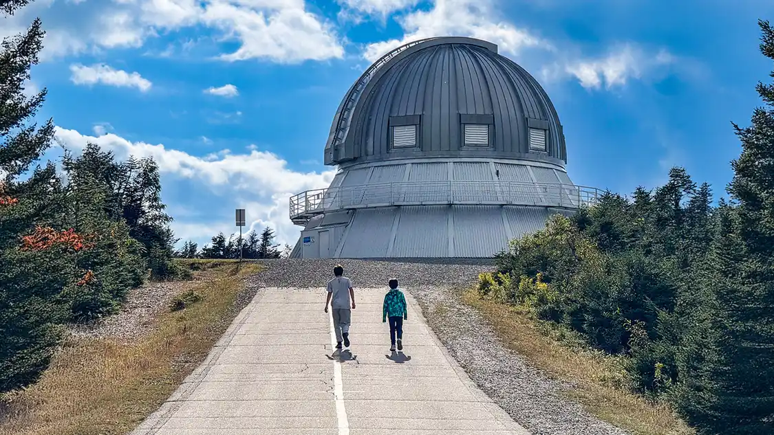 Two boys walk up a road toward a mountain-top observatory in Mont-Megantic National Park