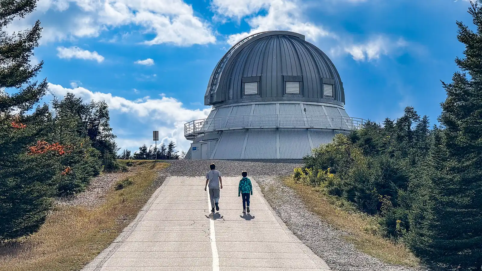 Two boys walk up a road toward a mountain-top observatory in Mont-Megantic National Park