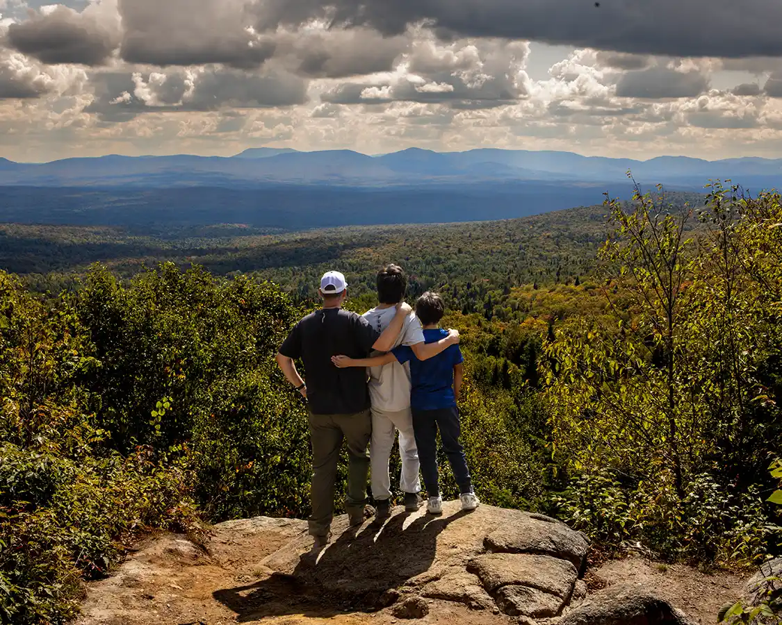 A father and his two sons pose at the top of a hiking trail looking out over the fall colors of Mont-Megantic National Park