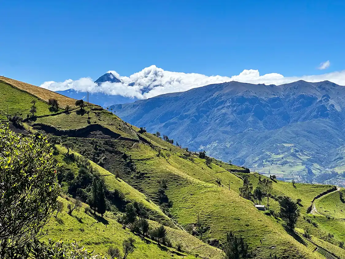 Glacier-topped mountains covered in clouds sit before green hills of the Andean mountains