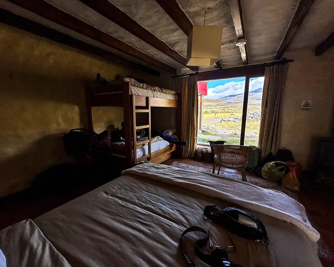 A rustic hotel room with a queen sized bed and bunk bed overlooking Cotopaxi volcano