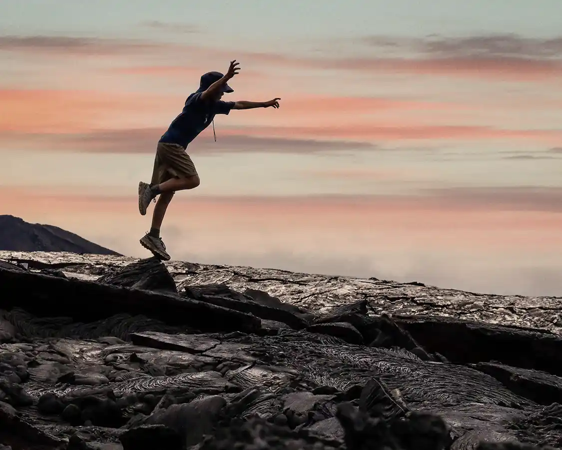 A boy hops over volcanic rocks at sunrise in the Galapagos Islands