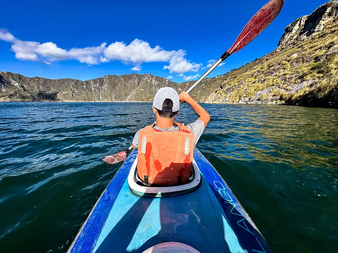 A teen boy paddles a kayak in a beautiful crater lake in Ecuador