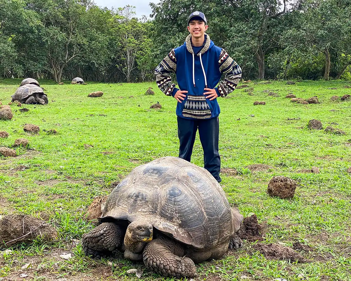 A teenager stands proudly behind a giant tortoise on Santa Cruz Island in the Galapagos
