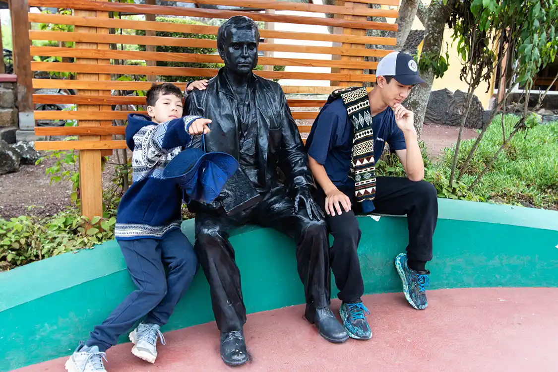 Two boys make a funny pose next to a statue of Charles Darwin at the Darwin Research Center on Santa Cruz Island, Ecuador
