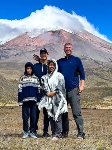 A family stands proudly beneath the cloud-covered glaciers of Cotopaxi Volcano in Cotopaxi National Park with kids