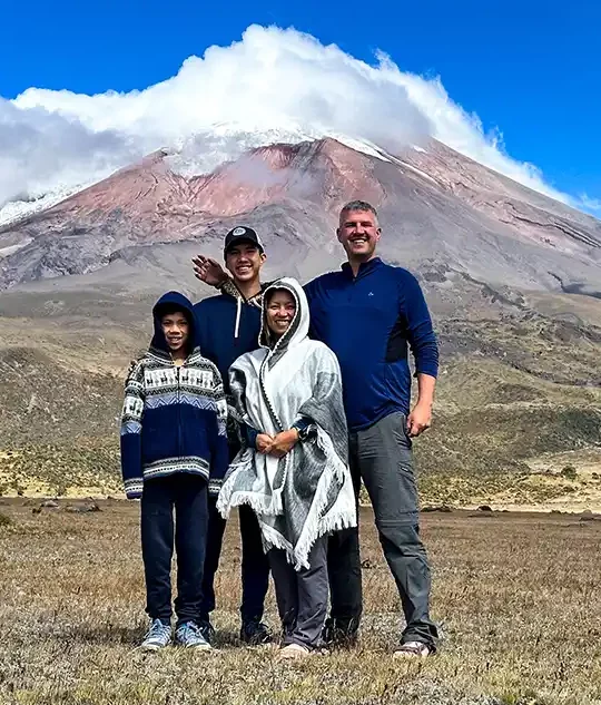 A family stands proudly beneath the cloud-covered glaciers of Cotopaxi Volcano in Cotopaxi National Park with kids