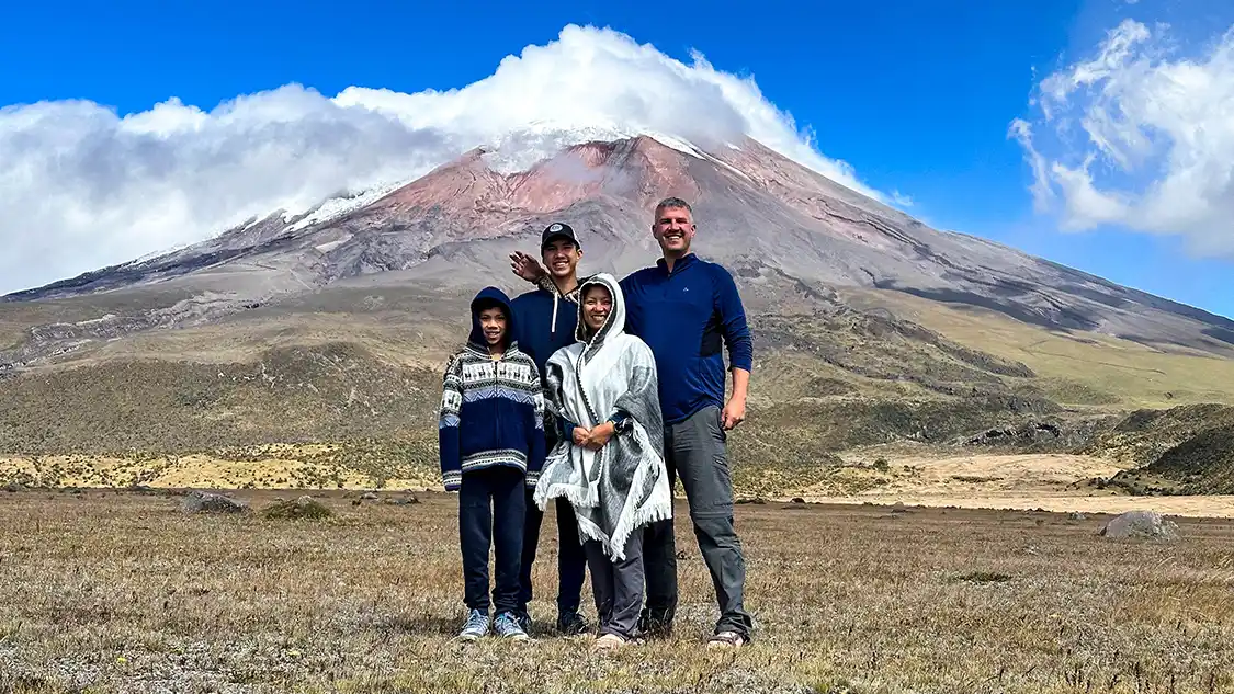 A family stands proudly beneath the cloud-covered glaciers of Cotopaxi Volcano in Cotopaxi National Park with kids