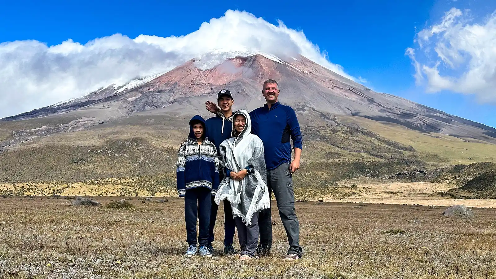 A family stands proudly beneath the cloud-covered glaciers of Cotopaxi Volcano in Cotopaxi National Park with kids